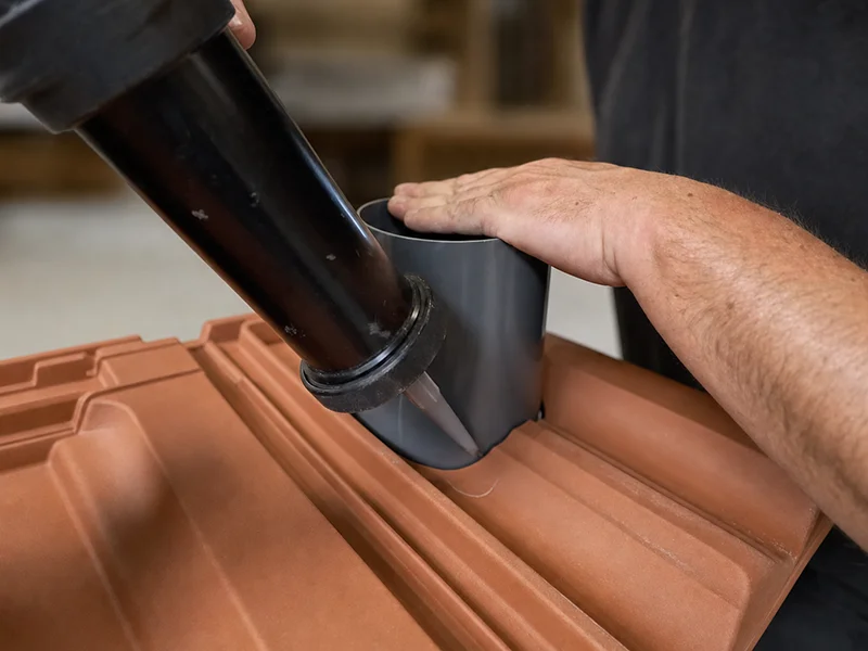 Rhedach Manufaktur: Grauer Rohrstutzen wird in einen terrakottafarbenen Original-Dachziegel eingeklebt